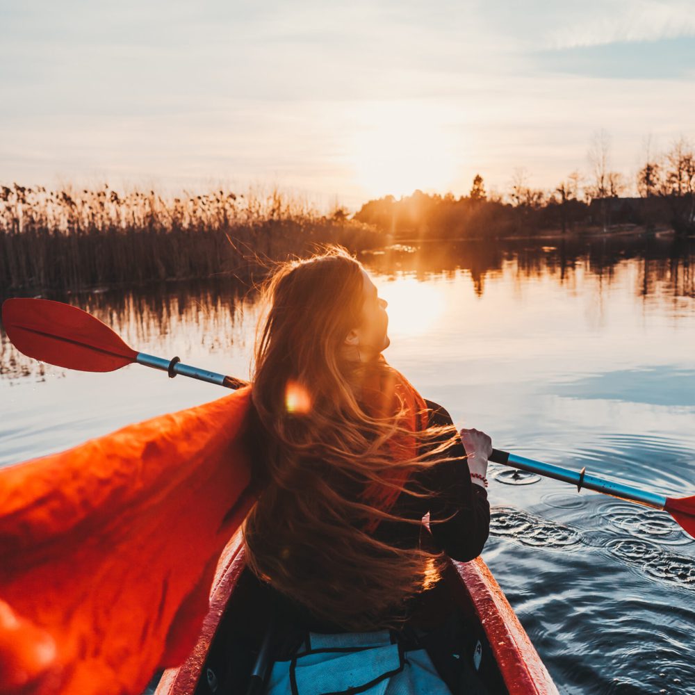 Back view of happy cute girl holding paddle in a kayak on the river, enjoying a lovely summer day
